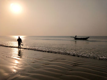 Silhouette man on beach against sky during sunset