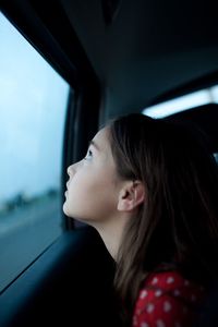 Side view of thoughtful girl looking through car window
