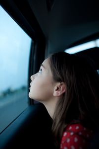 Side view of thoughtful girl looking through car window