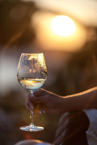 Close-up of woman holding wineglass against sunset