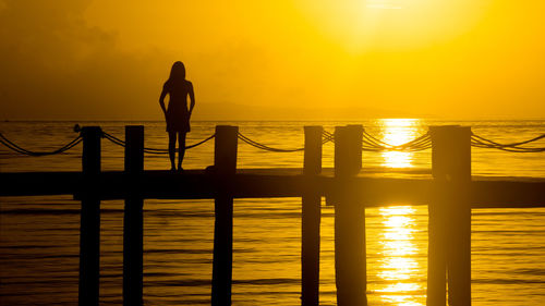 Silhouette man standing by sea against orange sky