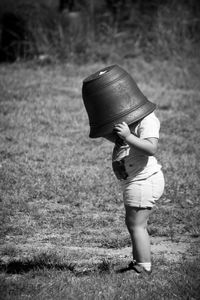 Side view of boy with bucket on head in grassy field