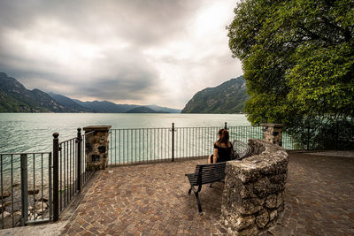 Woman sitting on seat by mountain against sky