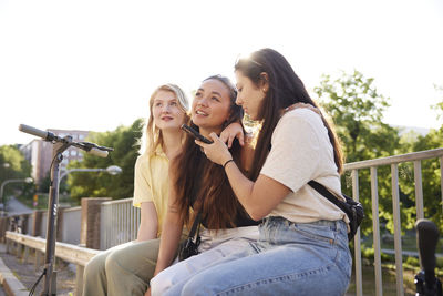 Young female friends spending time together outdoors and using phone