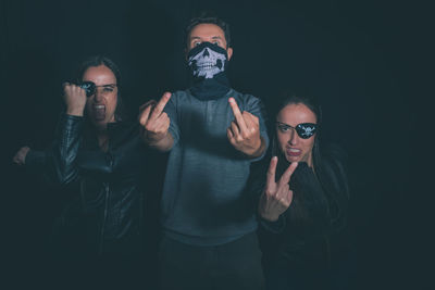 Portrait of friends wearing masks while standing against black background