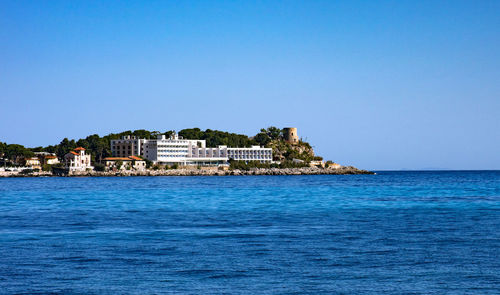 Building by sea against clear blue sky