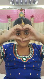 Portrait of smiling girl making heart shape while sitting in ceremony