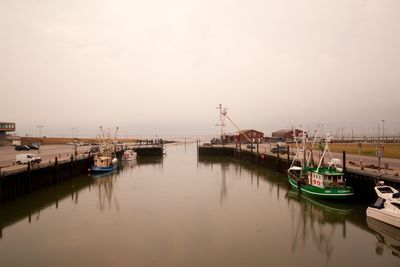 Boats moored at harbor in misty morning at low tide