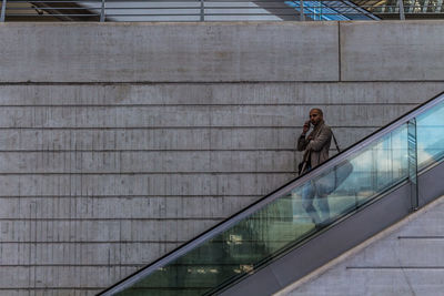 Businessman standing on escalator against wall