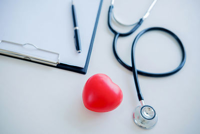 Directly above shot of heart shape and stethoscope with clipboard on gray background