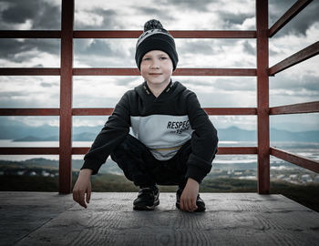 Portrait of boy standing on railing against sky