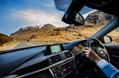 Cropped hand driving car on road amidst mountains