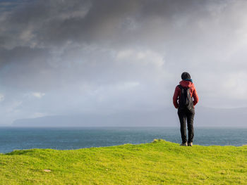 Rear view of man standing on sea shore against sky