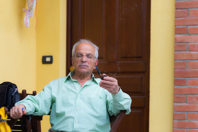 Portrait of man smoking pipe cigarette against house