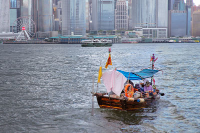 People sitting on boat in river with city in background