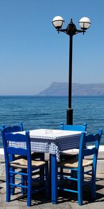 Empty chairs and table by sea against clear blue sky