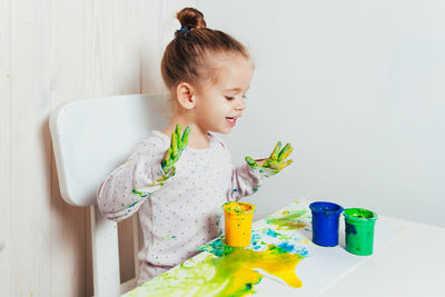 Cute baby girl sitting with paper and paints at table