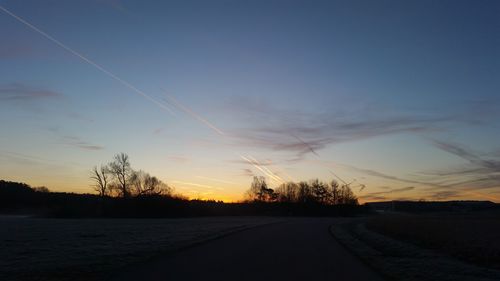 Road by silhouette trees against sky during sunset