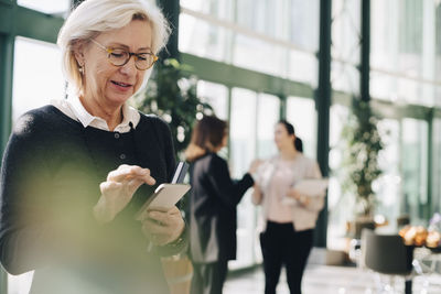 Senior entrepreneur using mobile phone while coworkers discussing in background