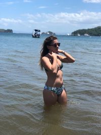 Young woman in bikini on beach against sky