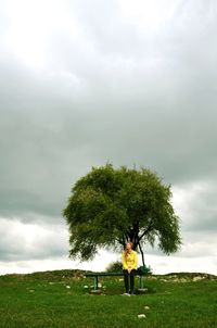 Full length of woman sitting on bench at grassy field against cloudy sky