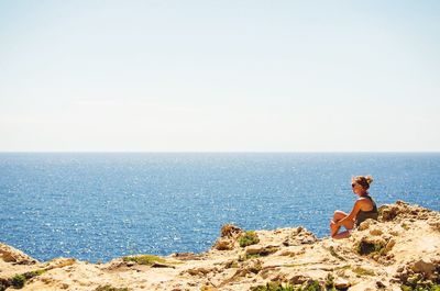 Young woman sitting on shore in front of sea during sunny day