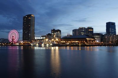 Illuminated buildings by river against sky at night