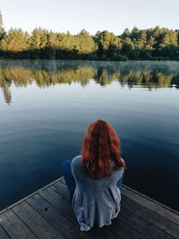 Rear view of woman sitting on pier over lake