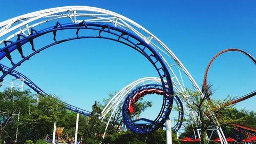 Low angle view of rollercoaster against clear blue sky