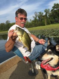 Portrait of mature man holding fish by dog in boat