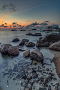Rocks on beach against sky during sunset