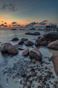 Rocks on beach against sky during sunset