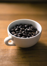 Close-up of roasted coffee beans in cup on hardwood floor