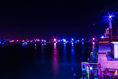 Illuminated city by sea against sky at night