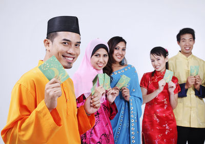 Portrait of happy friends in traditional clothing holding envelopes against white background