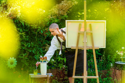 Beautiful woman relaxing while painting an art canvas outdoors in her garden. creativity concept.