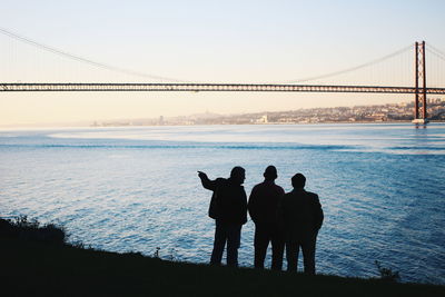 Silhouette male friends standing together by sea against sky