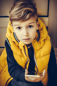 Small kid relaxing outdoors while using cell phone and looking at camera.