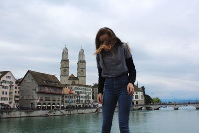 Woman standing by river with city in background