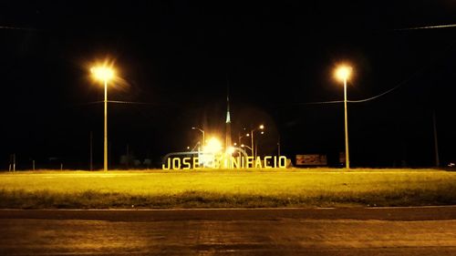 Illuminated street lights by road against sky at night