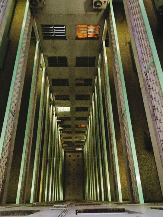 architecture, built structure, the way forward, indoors, diminishing perspective, in a row, ceiling, low angle view, building exterior, building, architectural column, corridor, illuminated, column, vanishing point, narrow, steps, empty, railing, lighting equipment