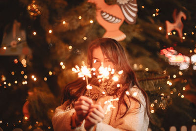 Happy teenage girl holding sparklers standing by christmas tree