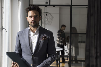 Portrait of confident salesman holding folder while standing at home