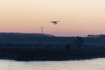 Silhouette airplane flying against sky during sunset