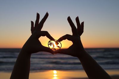Close-up of hand holding sea against sky at sunset