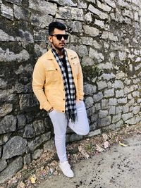 Young man wearing sunglasses standing against wall