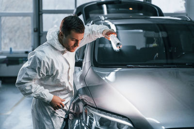 Silver colored car. man in uniform is working in the auto service.