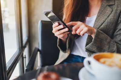 Midsection of businesswoman using mobile phone while having coffee at restaurant