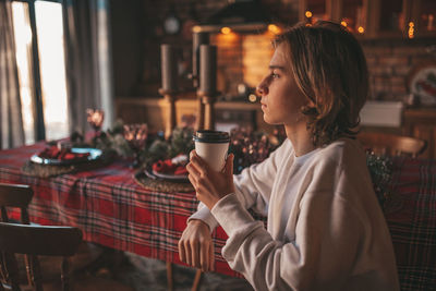 Portrait of candid authentic smiling handsome boy teenager using mobile phone at xmas home interior