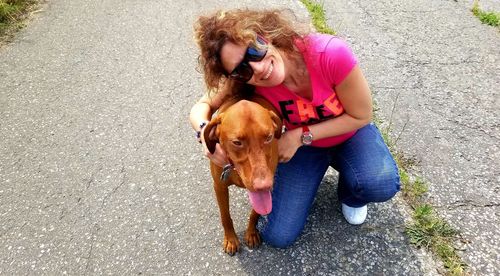 Portrait of smiling woman with dog kneeling on road